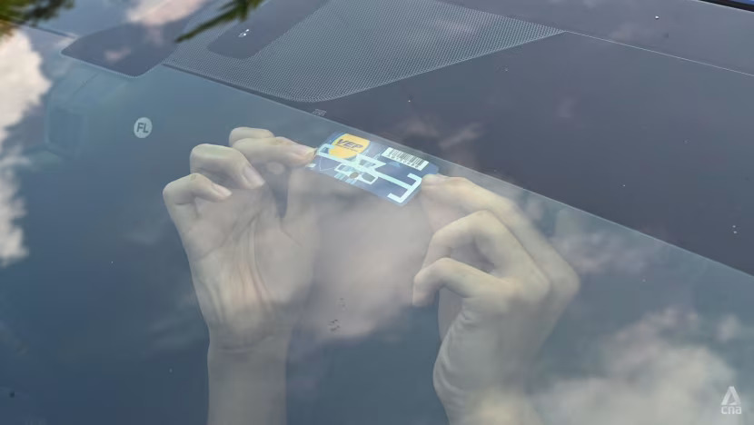 A technician installing a Vehicle Entry Permit RFID tag on the windshield of a Singapore-registered car.